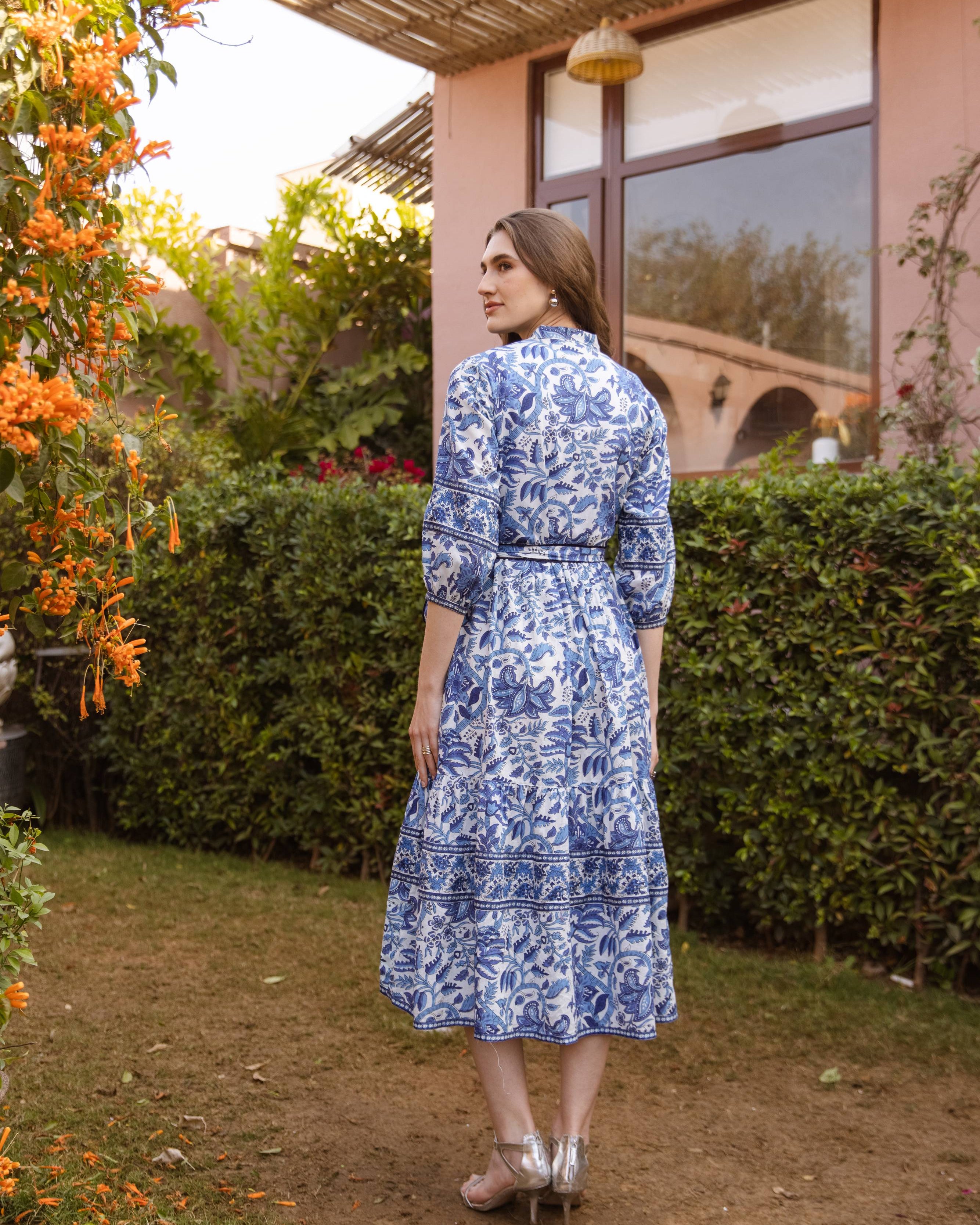 Woman in a blue floral dress standing in a garden with a building in the background