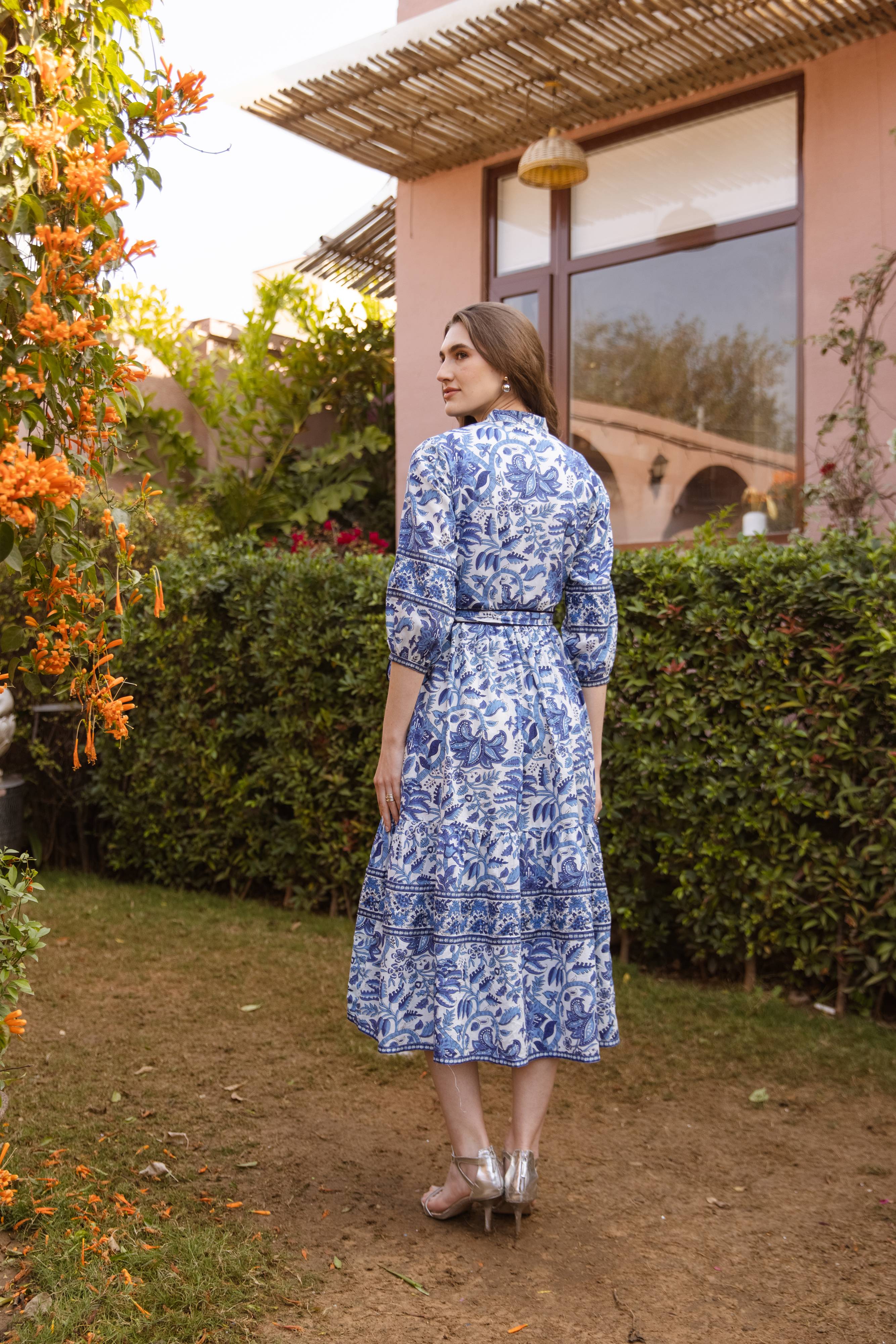 Woman in a blue floral dress standing in a garden with a building in the background