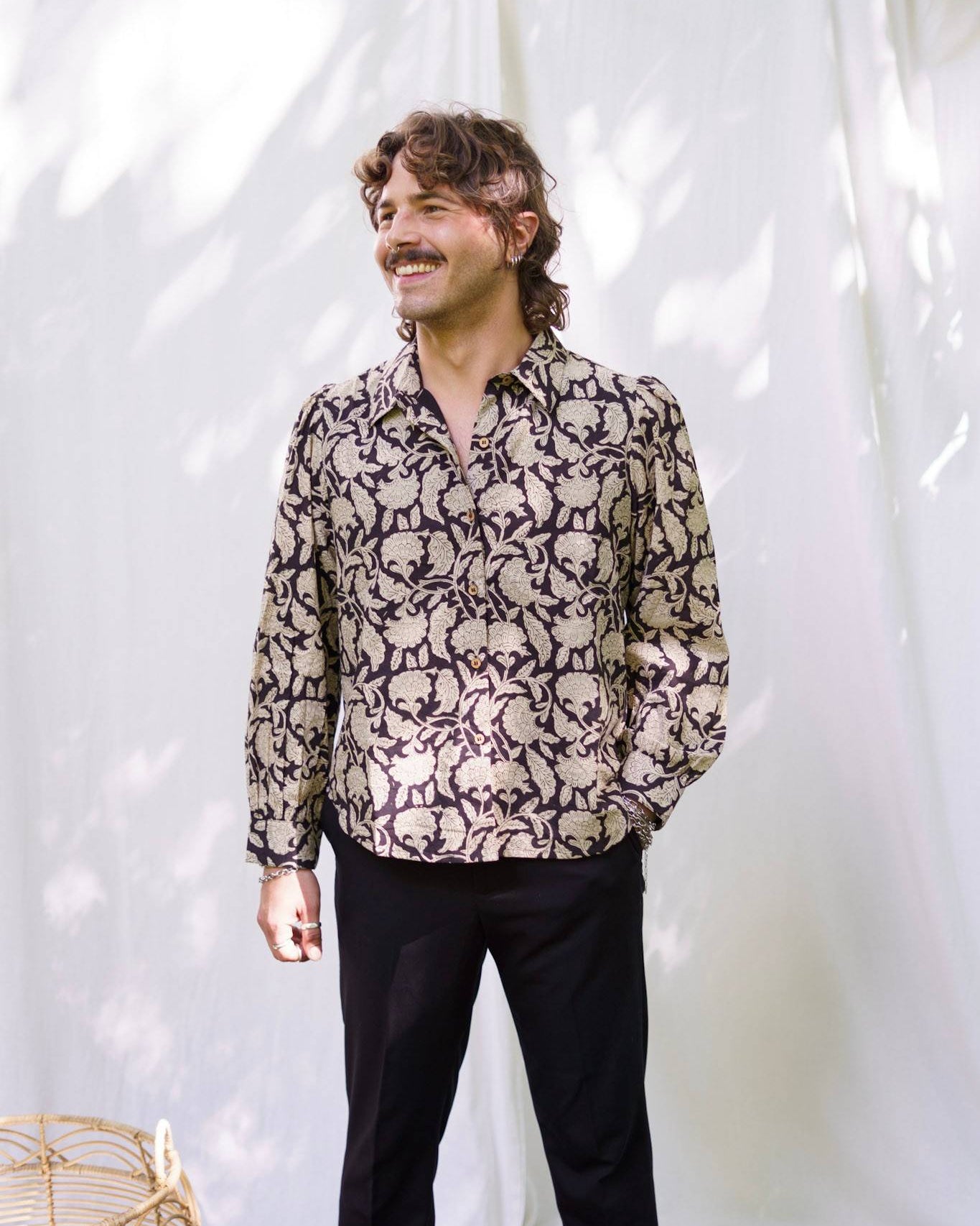 Man wearing a patterned shirt and black pants against a white background