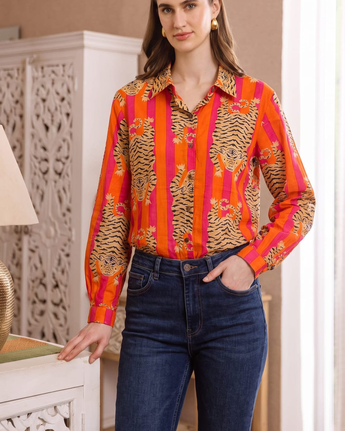 Full-length front three-quarter view of the Tibetan Tiger Blouse with one hand in jeans pocket, showing the orange and pink tiger print and blouse fit at the waist