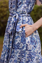 Blue and white floral dress with a belt, worn by a person outdoors.The dress has a pocket and the person showcases the pocket feature.
