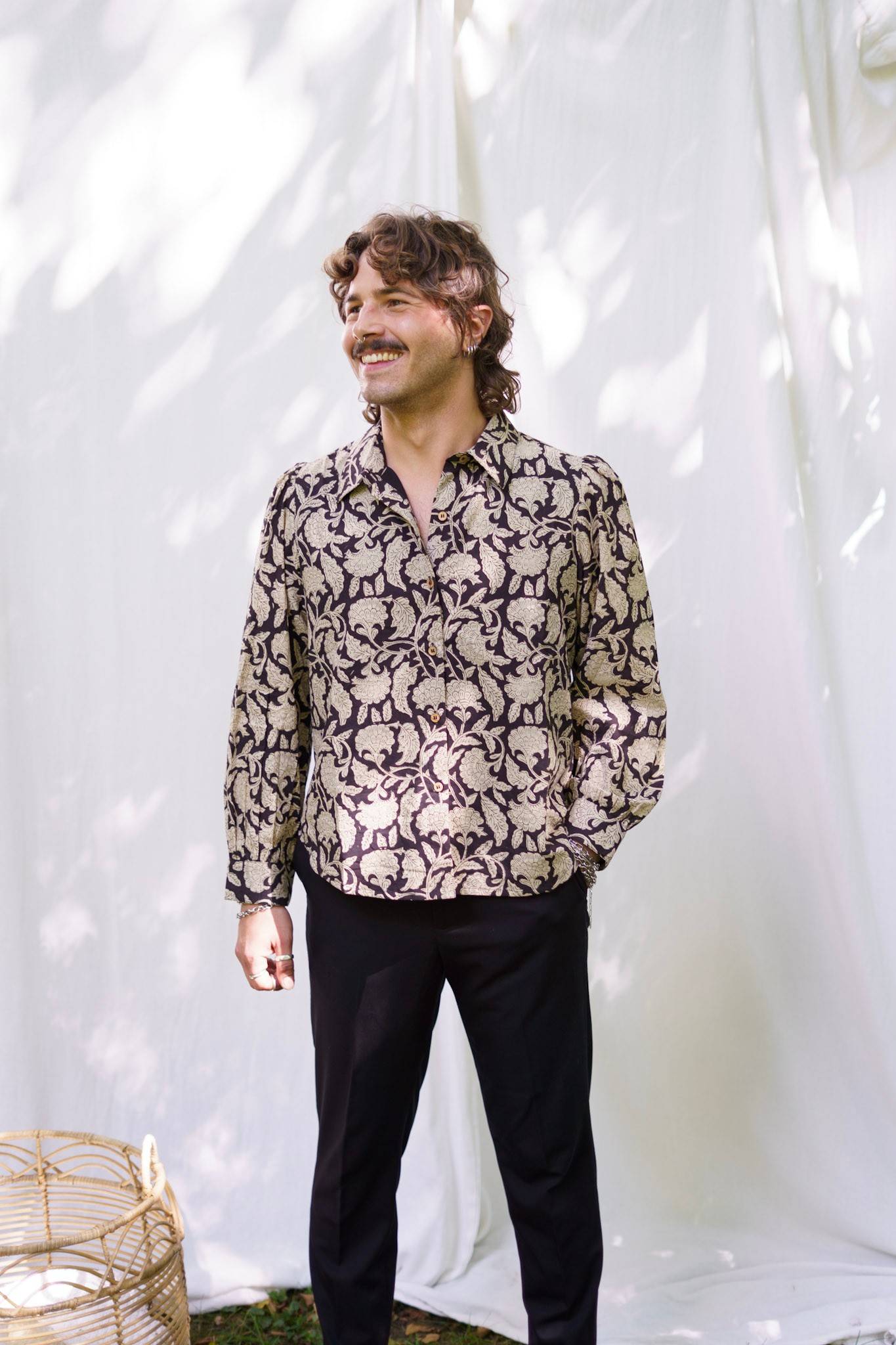 Man wearing a patterned shirt and black pants against a white background