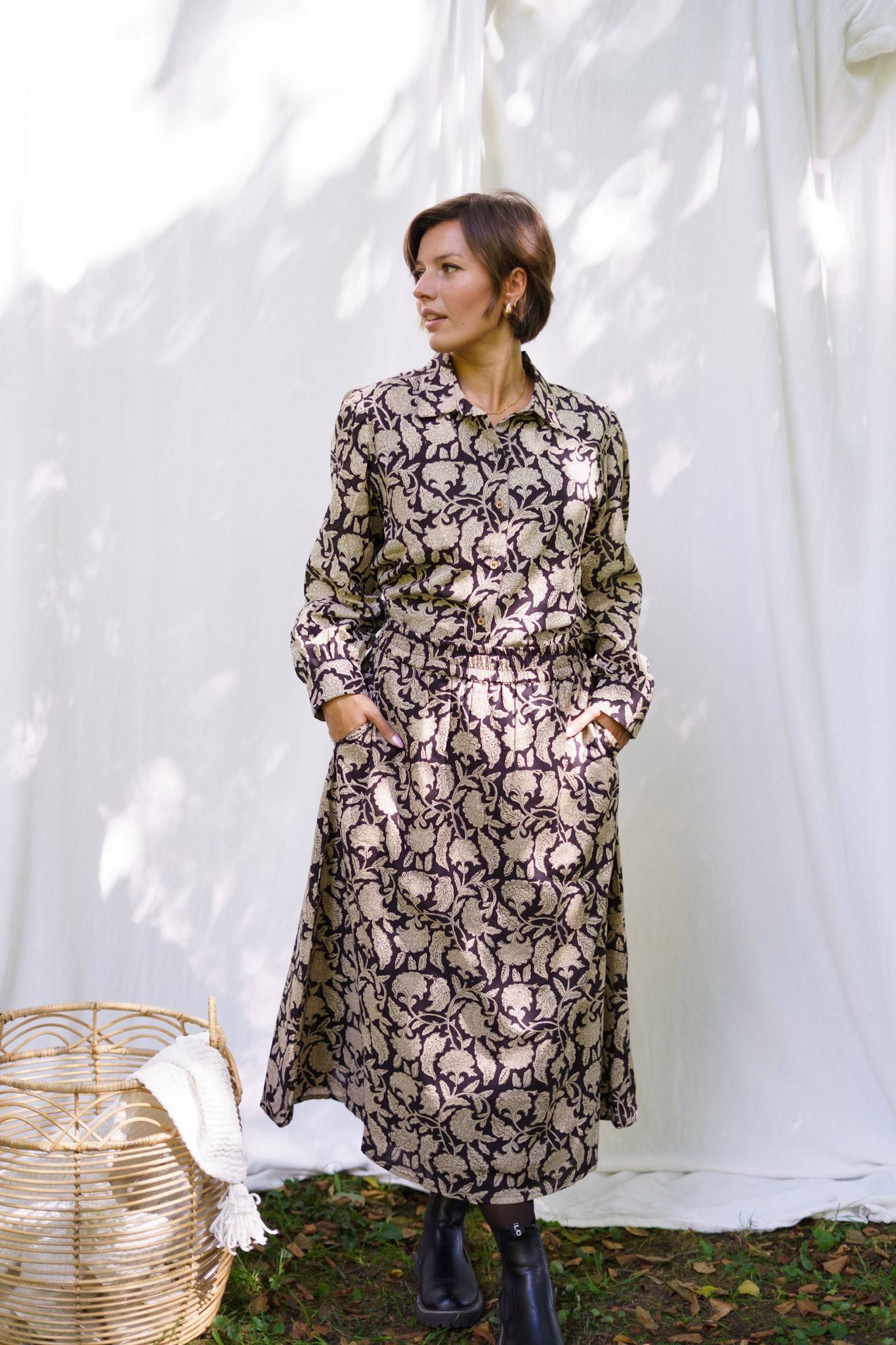 Woman wearing a long, patterned dress standing against a white curtain.