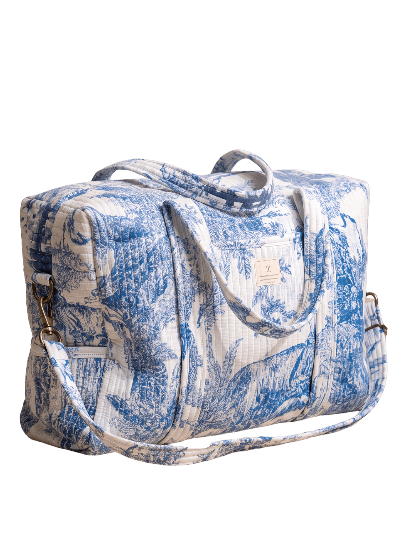 Three-quarter side view of the blue and white safari toile quilted duffel bag with both top handles raised and gingham crossbody strap draped in front, showing the fabric brand label