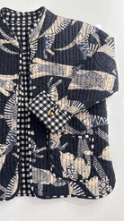 Close-up flat lay of Blue Cat Chaos Jacket showing quilted cotton texture, navy and cream cat print, gingham cuff, wooden toggle button, and patch pocket detail