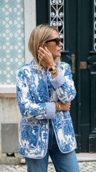 Close-up front view of the Blue Jardin Jacket showing the blue and white toile print, stand collar, and blue striped cuff, worn with sunglasses, a watch, and layered bracelets