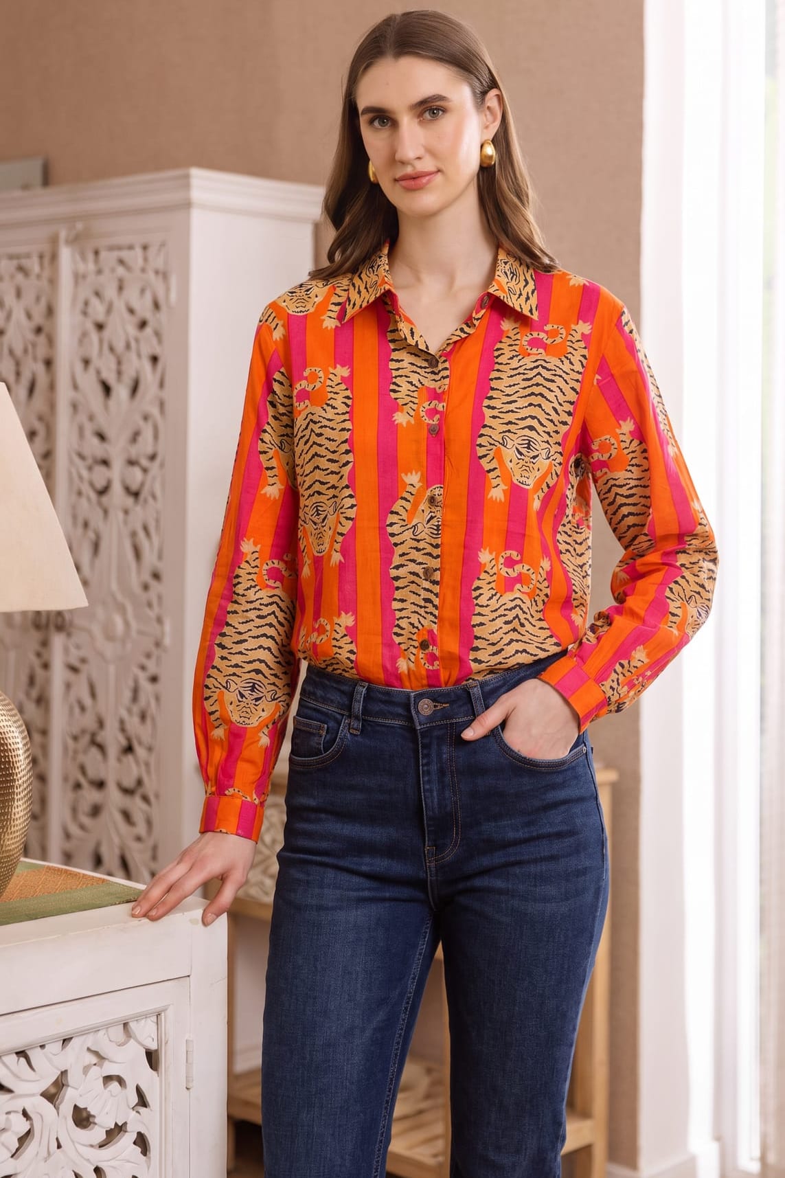 Full-length front three-quarter view of the Tibetan Tiger Blouse with one hand in jeans pocket, showing the orange and pink tiger print and blouse fit at the waist