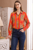 Full-length front three-quarter view of the Tibetan Tiger Blouse with one hand in jeans pocket, showing the orange and pink tiger print and blouse fit at the waist